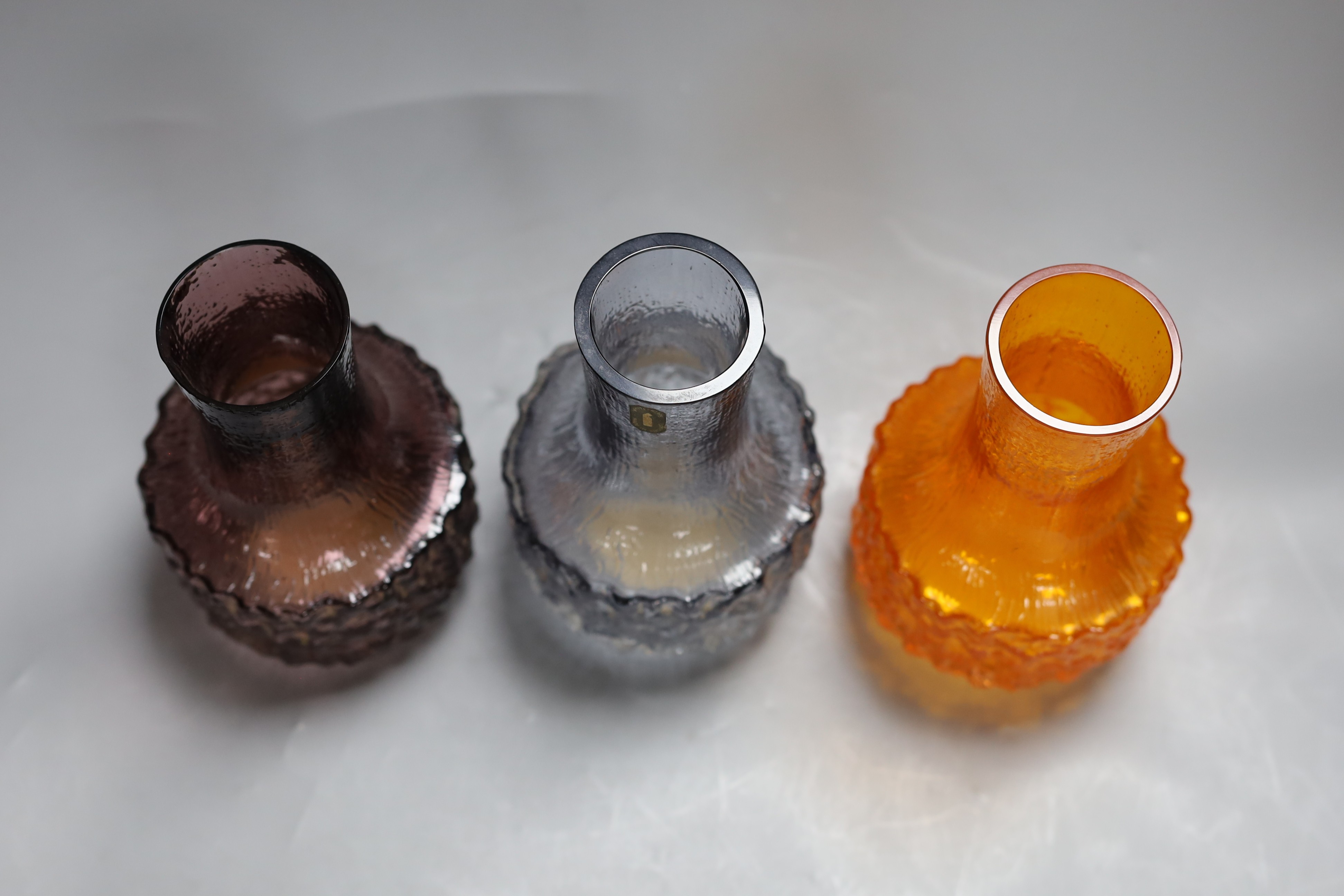 Three Whitefriars cylindrical bottle vases, in amethyst, tangerine and smoked glass, each 18cm high.
